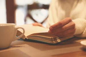 Woman,With,Coffee,Reading,Book,At,Wooden,Table,,Closeup