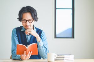 Young,Man,Reading,A,Book,In,His,Study,At,Home