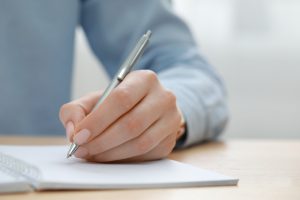 Woman,Writing,In,Notebook,At,Wooden,Table,,Closeup