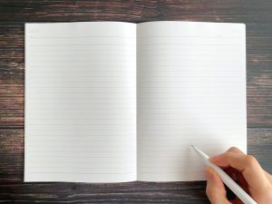 Woman's,Hand,Holding,An,Open,Notebook,And,A,Ballpoint,Pen
