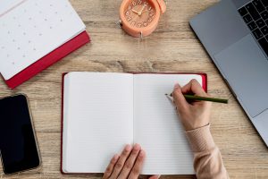 Close-up,Of,A,Hand,Writing,In,An,Notebook,On,Wooden